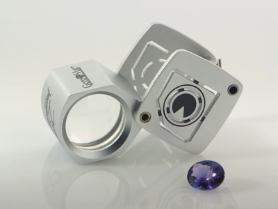 A gemologist loupe is placed near a dark blue polished and faceted gemstone.