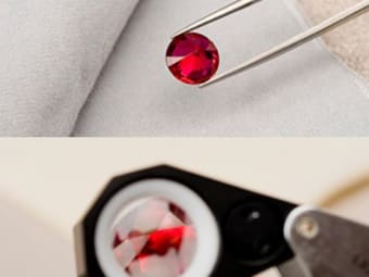 A gemstone tweezer and loupe are used to inspect a red gemstone.