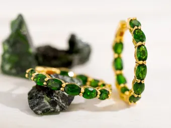 Chrome diopside gold earrings are featured in front of chrome diopside
rough specimens.