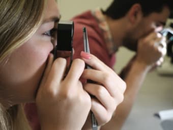 A woman views a green gemstone through a loupe.